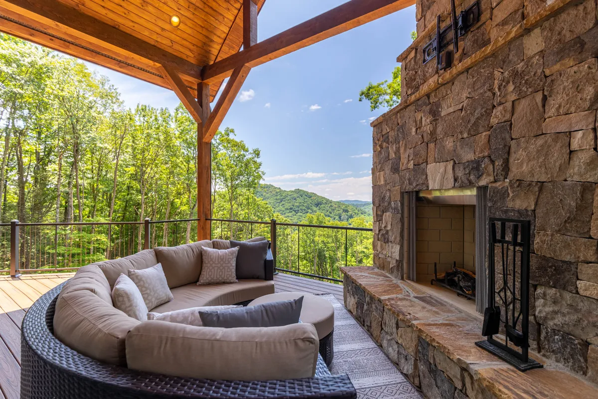 A curved stone seating area surrounds a cozy outdoor fireplace set against a backdrop of mountain views. The space is designed for gathering, with ample room for families to relax, roast marshmallows, or share stories by the fire. The natural surroundings and tranquil atmosphere invite outdoor enjoyment.