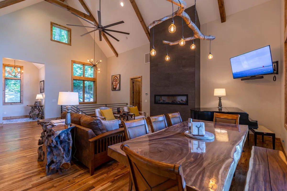 An inviting open-plan dining and living area with a large wooden dining table, modern pendant lights above, a cozy sofa area, and a fireplace. The layout encourages both dining and lounging, with ample room for groups to gather and relax together.