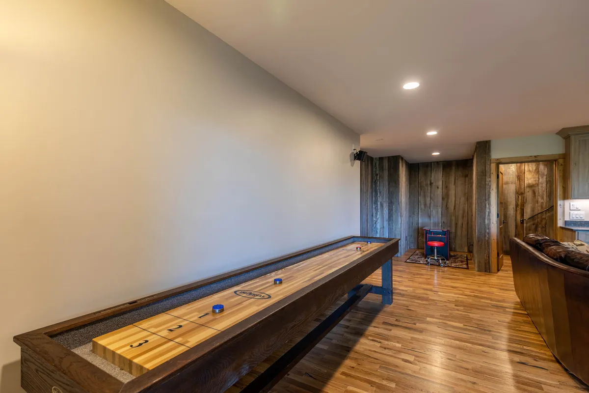 This image features a shuffleboard table set against a wooden wall, with a comfortable seating area nearby. The overall mood is playful and relaxed, inviting friendly competitions and socializing.