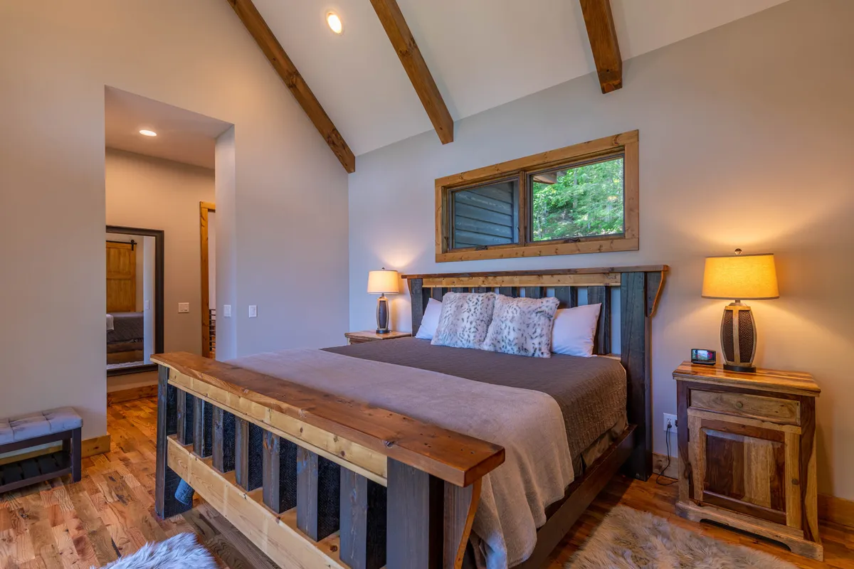A calm and serene bedroom with a wooden bed, decorative pillows, and soft lighting provided by bedside table lamps. The tranquil color palette and simple decor offer an inviting space for peaceful rest.