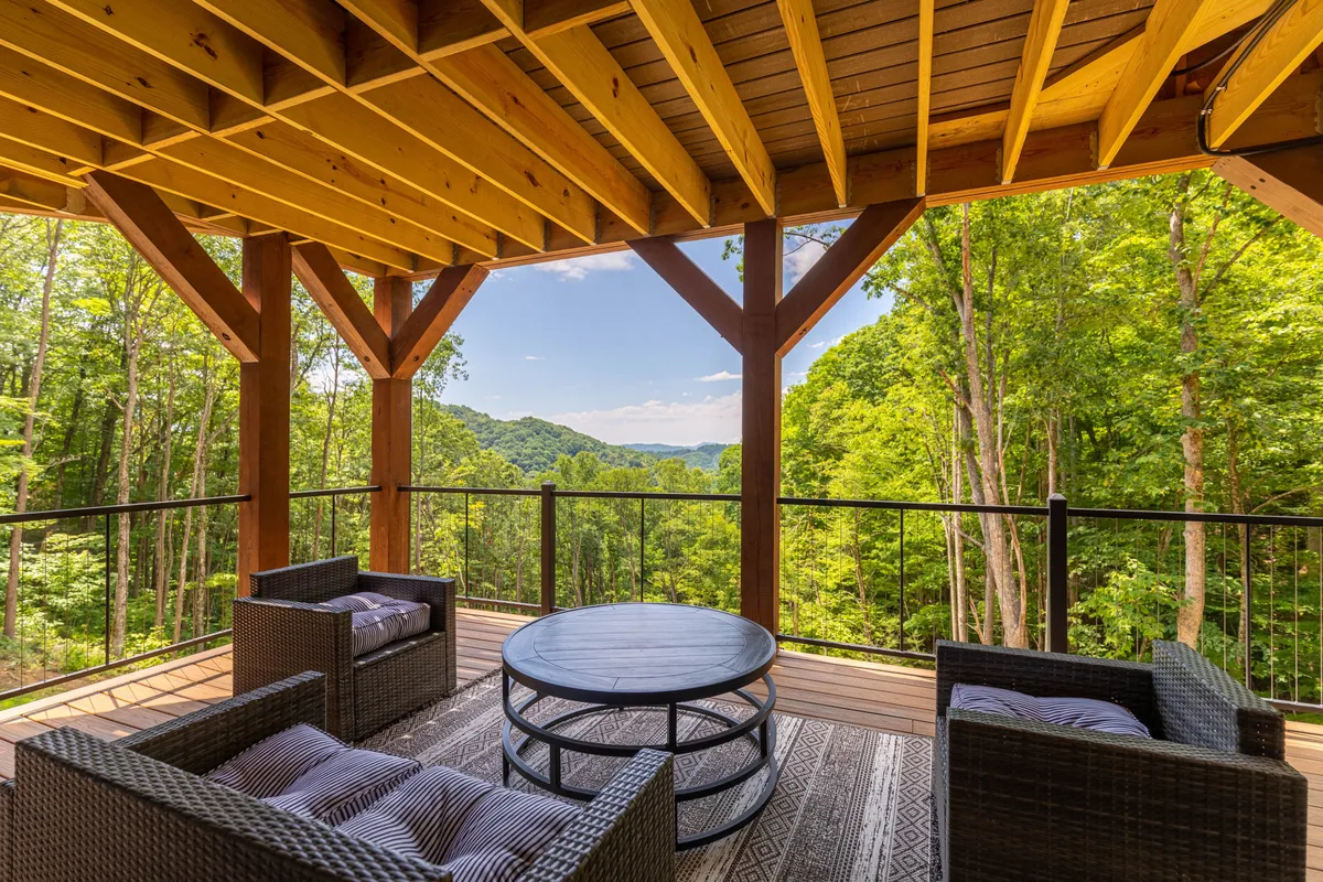 An inviting outdoor seating area faces a panoramic view of the mountains, framed by sturdy wooden beams. The space is perfect for relaxing, socializing, and taking in nature's beauty, especially at sunrise or during evening stargazing.
