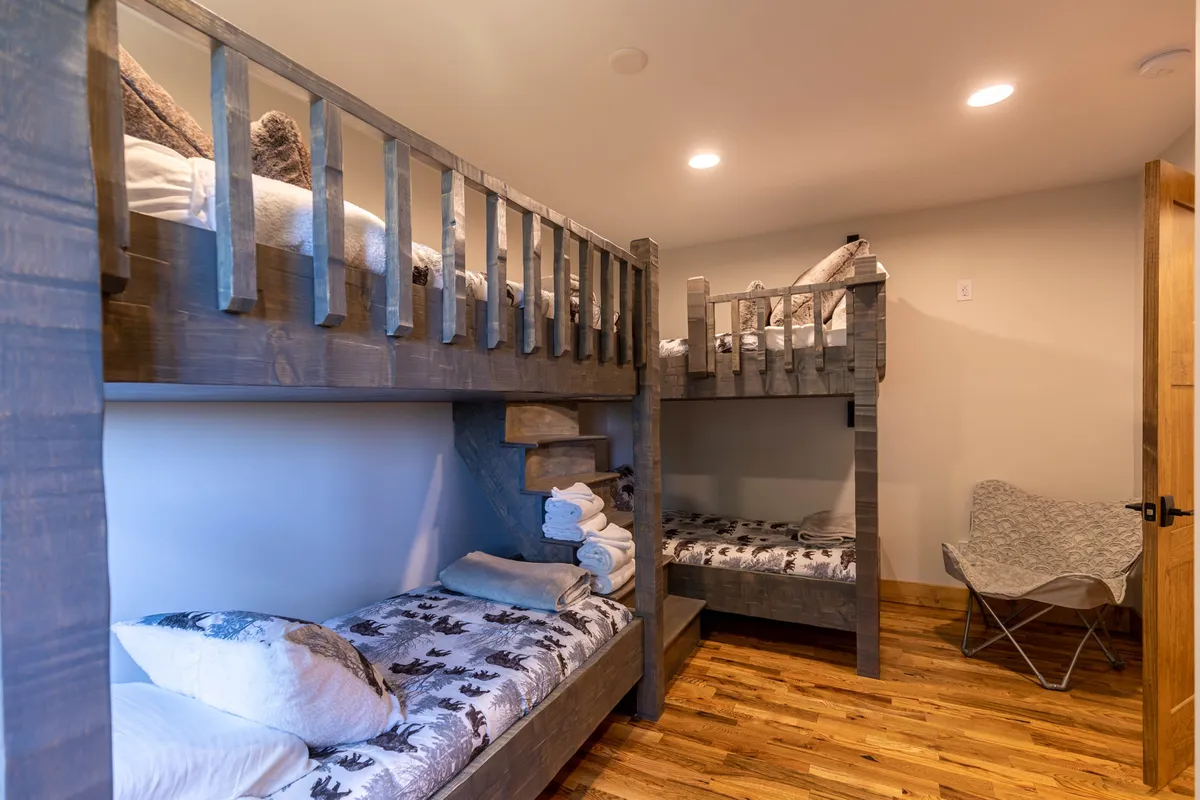 A cozy bunk room with built-in bunk beds, textured bedding, and warm wooden flooring. The playful setup encourages both restful sleep and fun, ideal for children and young guests.