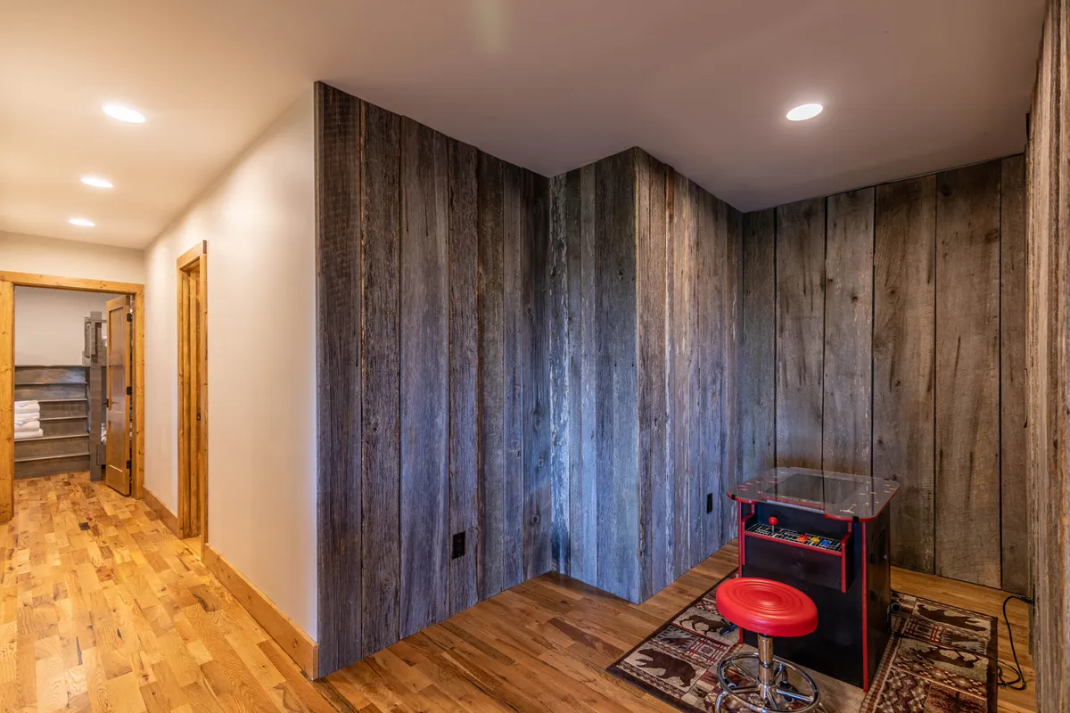 A cozy arcade area with a classic arcade game table and a vibrant red stool, set against warm wooden textures. The setting evokes nostalgia and encourages fun-filled gatherings.